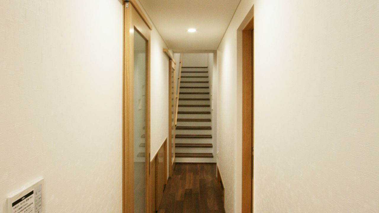 白い壁の廊下の先に、木の踏み板の階段が見えます