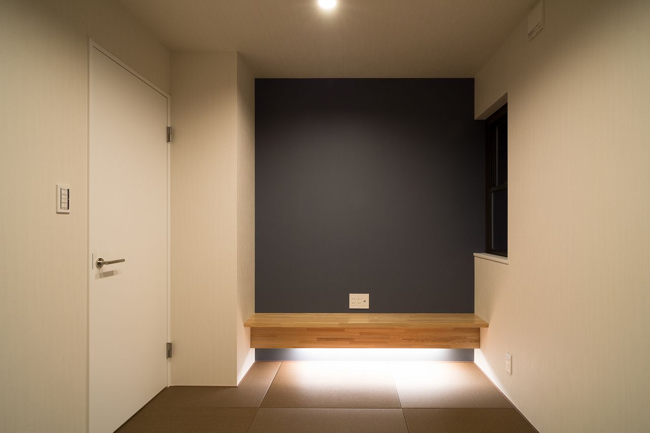 濃色の壁の前に木の板を浮かせ、足元を照らした畳の間